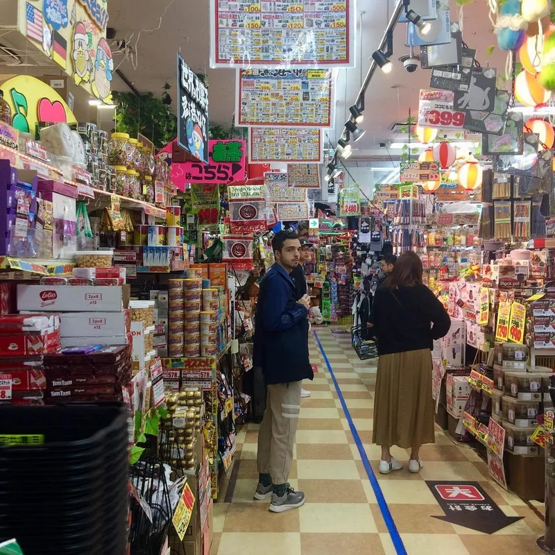 A person browsing the packed aisles of a Japanese discount variety store filled with colourful signs and products