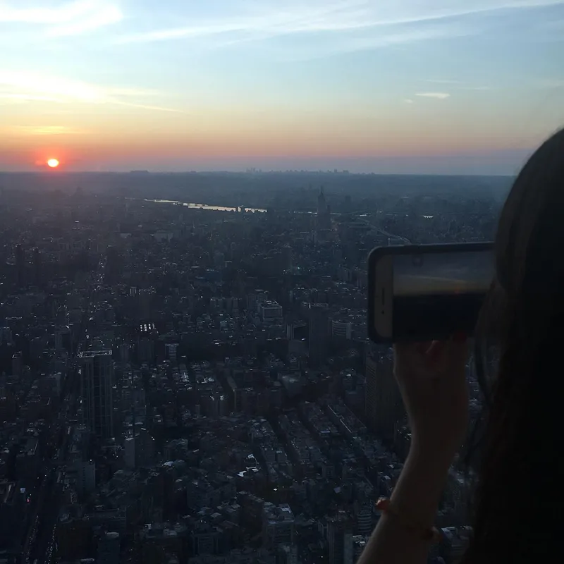 A person photographing the sunset over Taipei's vast cityscape from the top of Taipei 101