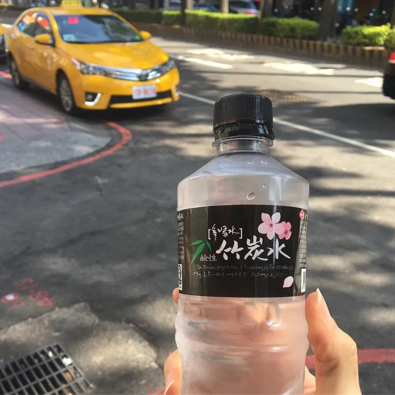 A hand holding a bottle of Taiwanese bamboo charcoal water with a yellow taxi in the background
