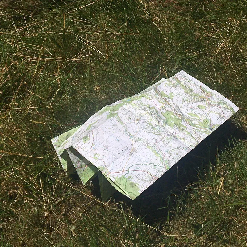 A folded topographic hiking map resting on grass