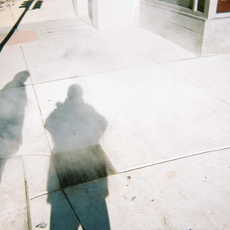 Shadow of a person with a camera cast on a sunlit concrete sidewalk