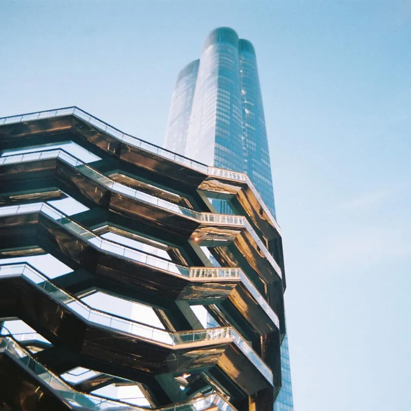 Looking up at the Vessel structure at Hudson Yards in New York City with a tower behind it