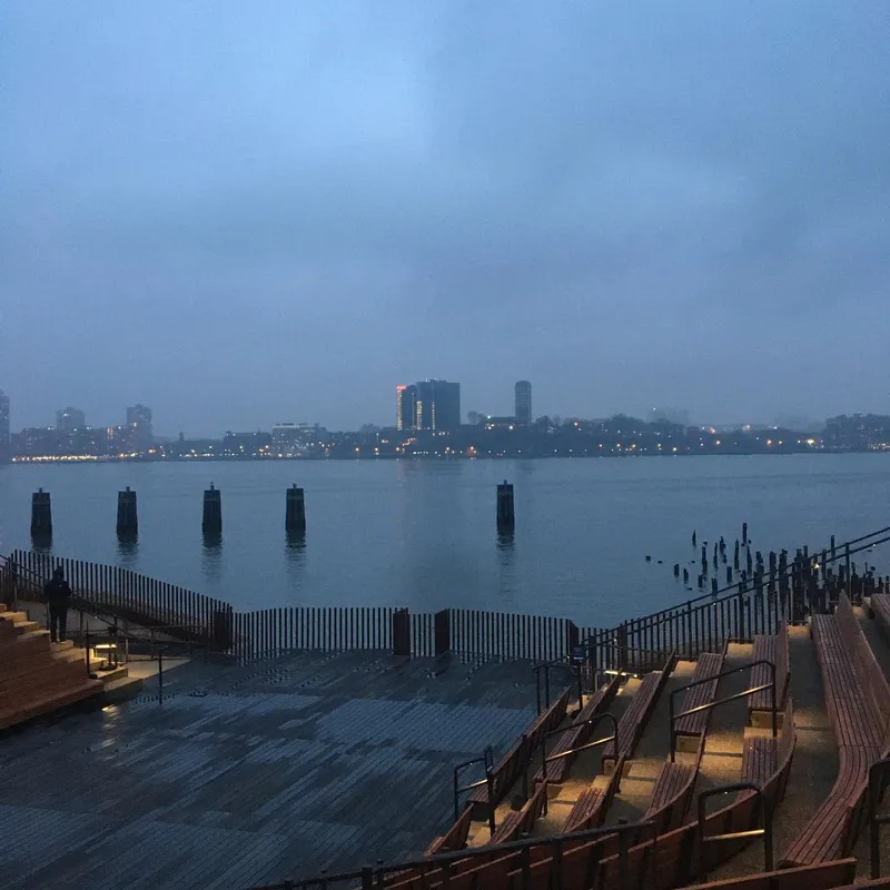 Rainy dusk view of the Hudson River from a waterfront pier with empty benches