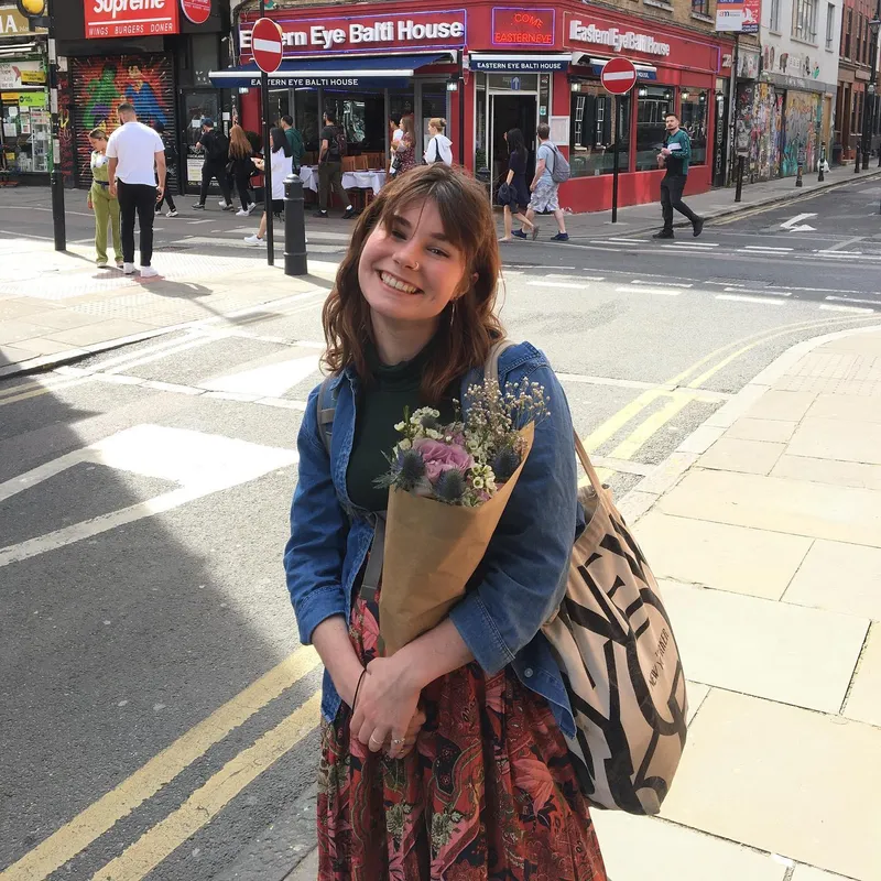 A smiling woman holding a flower bouquet on a busy East London street