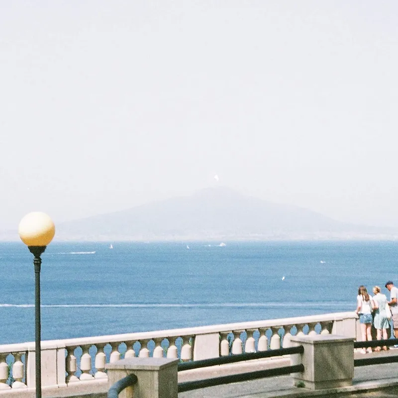 A waterfront promenade with a lamp post and a hazy island silhouette in the sea