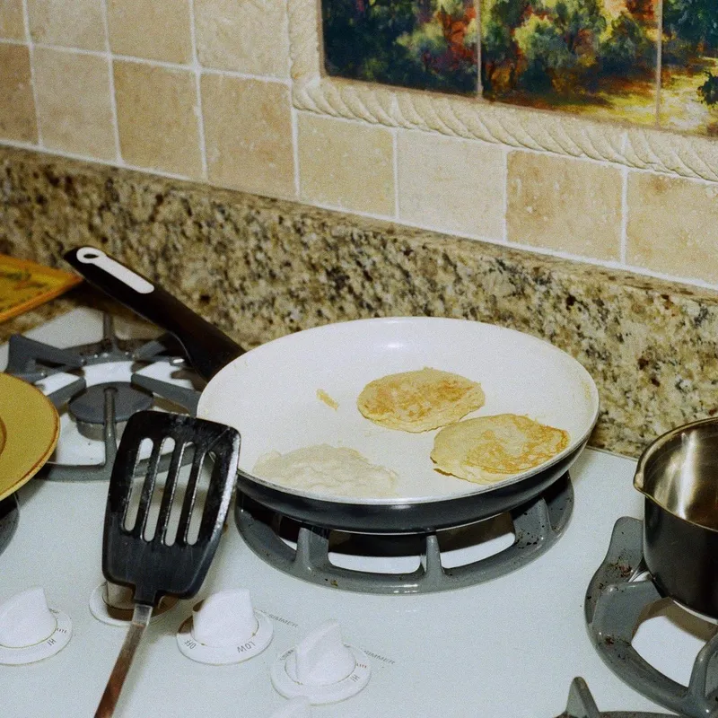 Three pancakes cooking in a white pan on a gas stove