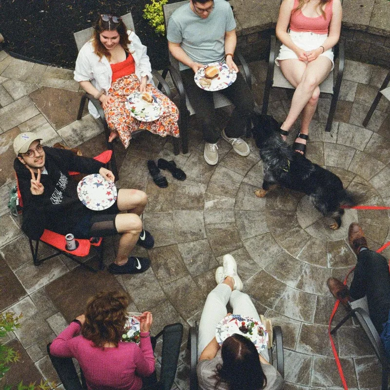 Overhead view of friends sitting in a circle on a patio with holiday plates and a dog