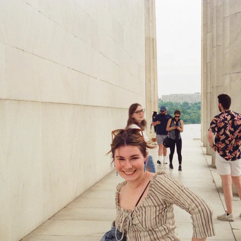 A smiling woman leaning forward between the marble columns of the Lincoln Memorial