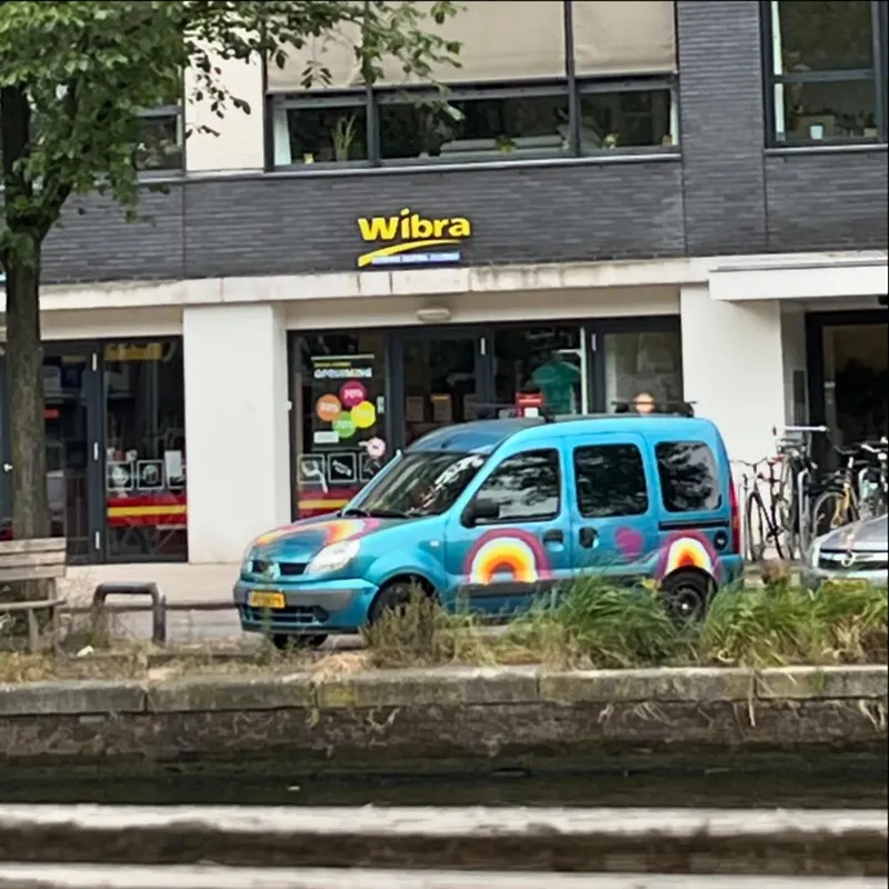 A colorful rainbow-painted Renault Kangoo parked by a canal