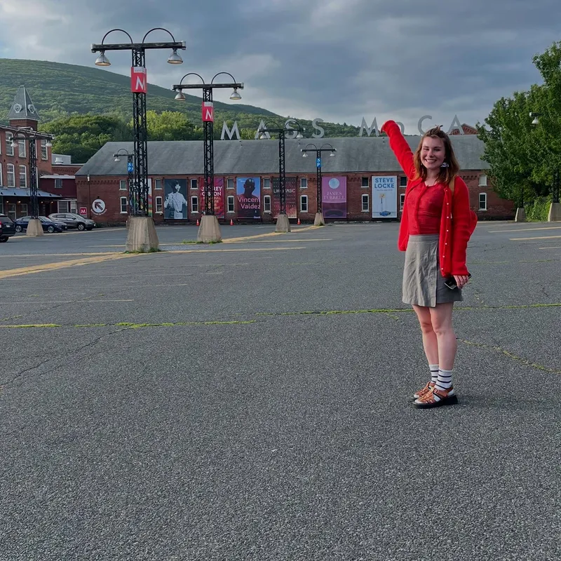 A young woman waving in front of MASS MoCA museum