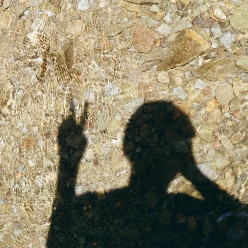 A person's shadow cast on a shallow rocky riverbed