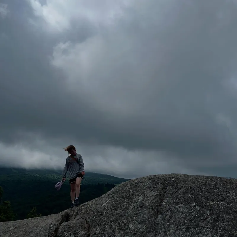 A hiker on a granite summit under stormy grey clouds