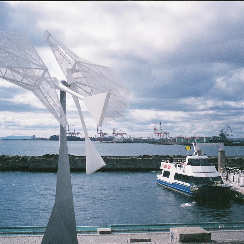A white geometric abstract sculpture at a Japanese harbor with a ferry docked next to it