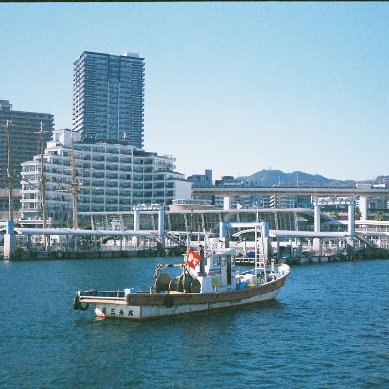A wooden fishing boat with a red flag crossing Kobe harbor