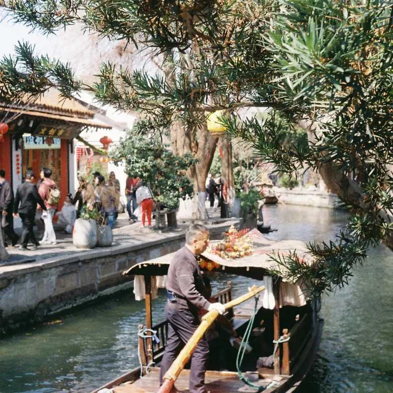 A boatman rowing a wooden canal boat through a traditional Chinese water town