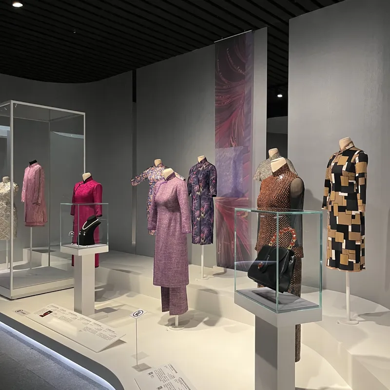 A gallery room displaying colorful modern qipao garments on mannequins with accessory cases