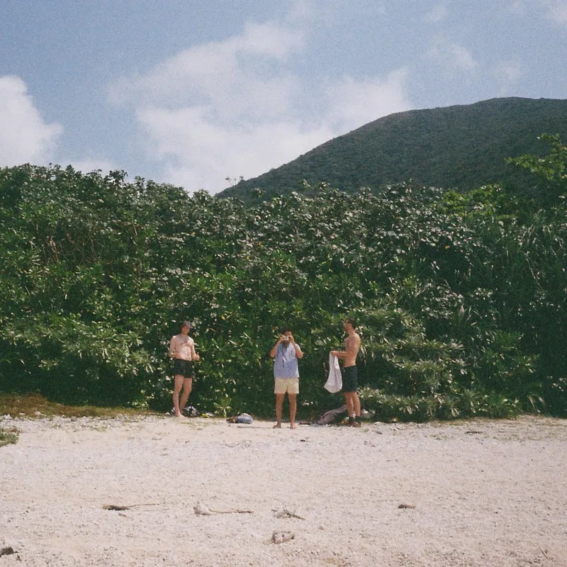 Three people standing on a remote white sand beach backed by dense jungle and a green hillside