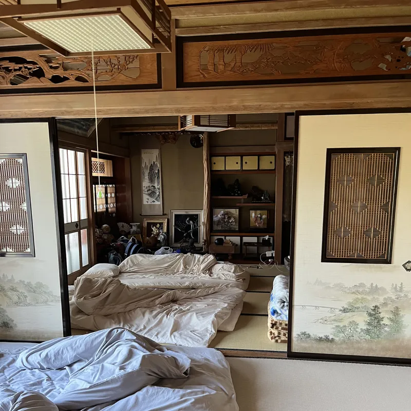 A traditional Japanese tatami room with futon bedding spread out and ornate carved wooden ceiling details