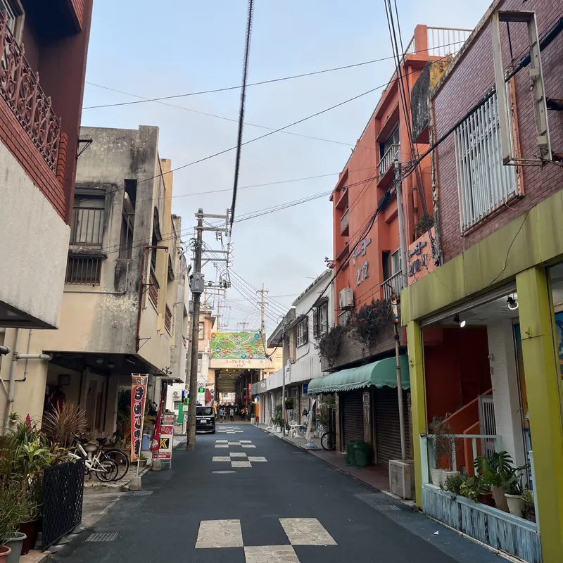 A quiet backstreet in Ishigaki with colorful low-rise buildings and overhead power lines leading to a covered market