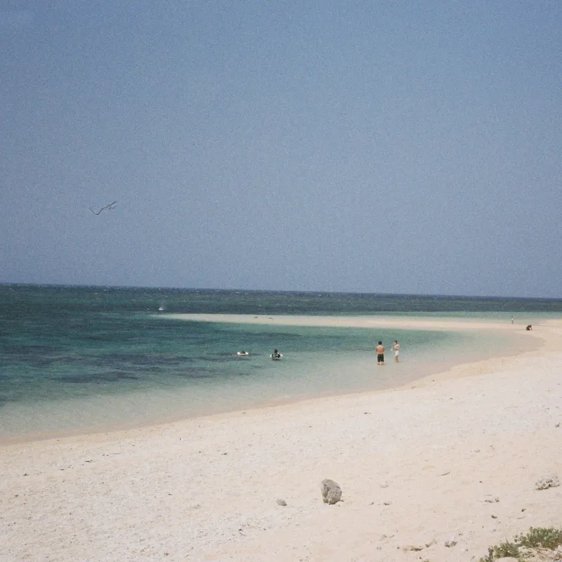 A white sand beach with turquoise water and a few swimmers on a clear day in Ishigaki, Okinawa
