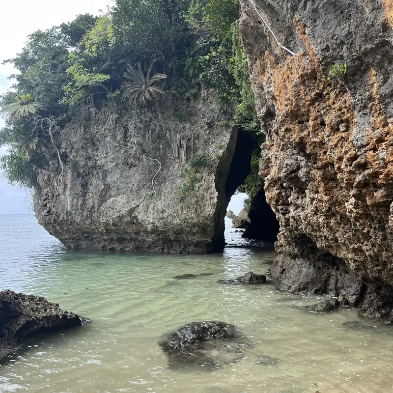 Rugged limestone sea cliffs with a natural arch and cave opening over clear teal water