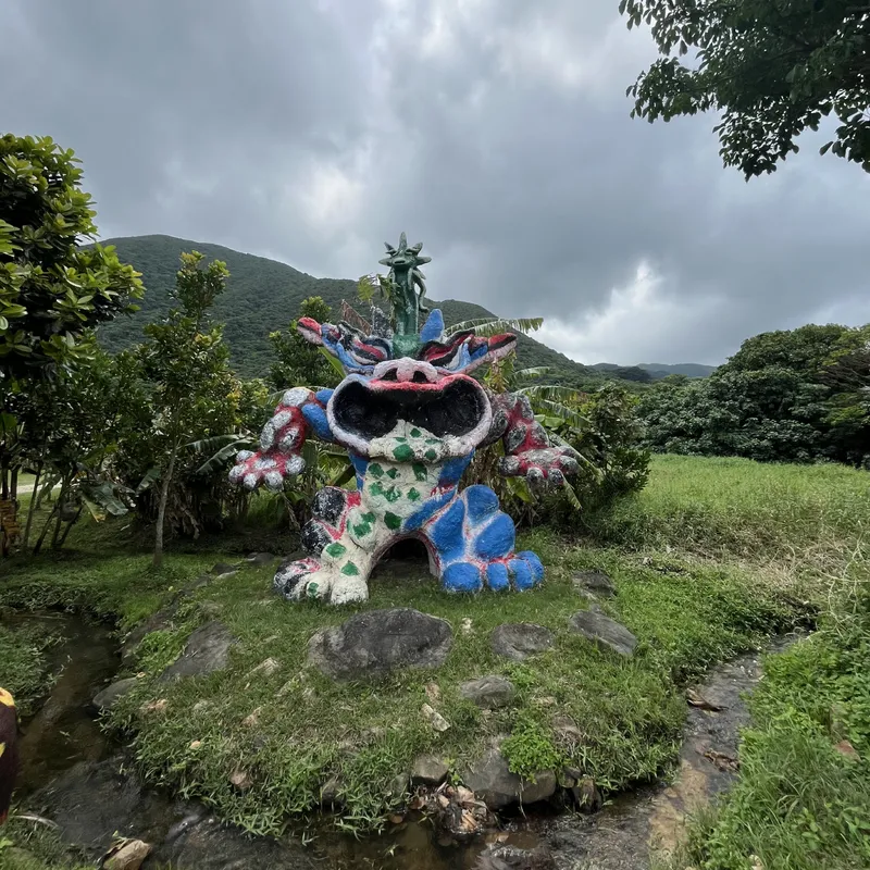 A colorful painted shisa monster sculpture on a grassy hillside under stormy skies in Okinawa