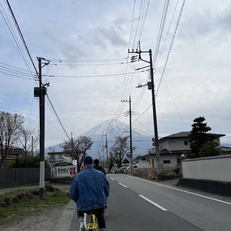 A cyclist riding toward snow-capped Mount Fuji along a quiet Japanese suburban road