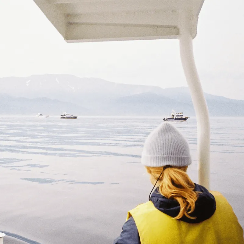 Woman with her back to the camera, wearing a yellow life jacket, gazing at the perfectly calm sea