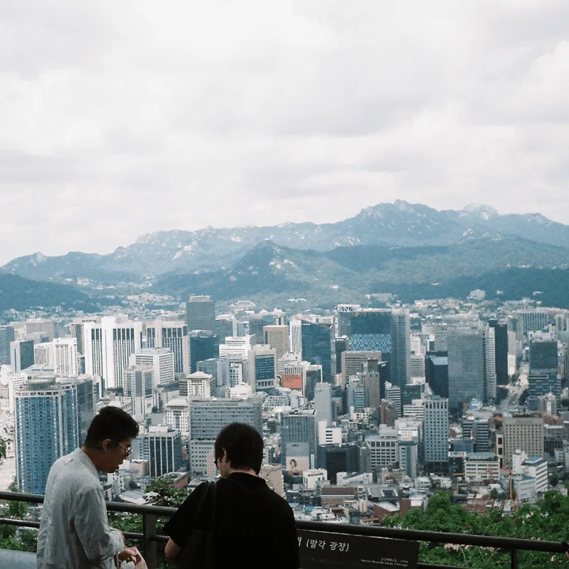 Two men chatting in front of a panoramic view of Seoul